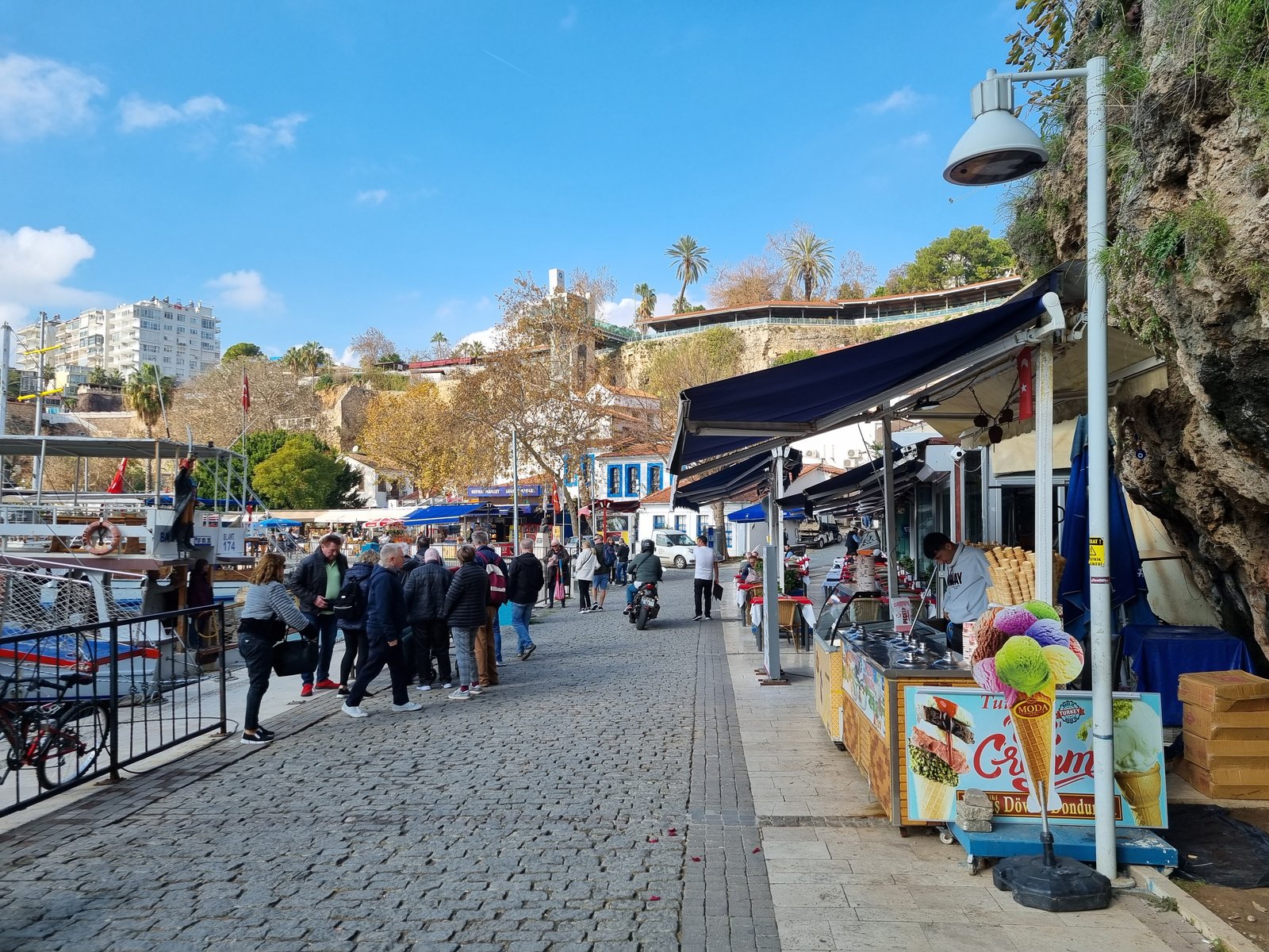 Visitors in jackets walking along the old harbour promenade in Antalya on a sunny January day